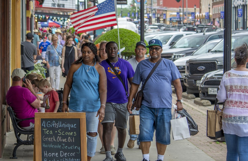 A woman and two men are walking out front of a local storefront.