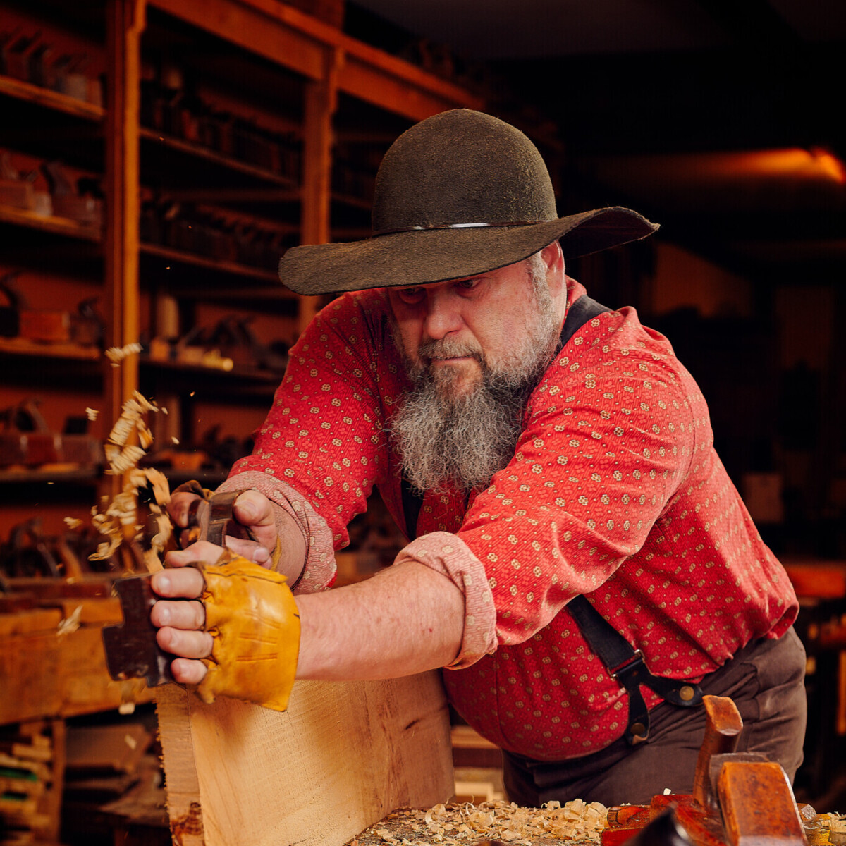 Bearded man is shaving wood intently to create hand-made furniture.