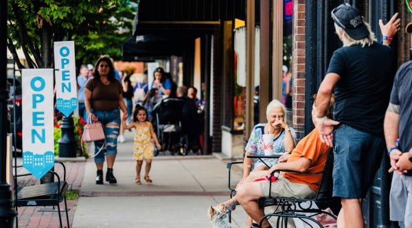 People walk, talk, and relax outside open businesses along a lively Main Street sidewalk in Bardstown, Kentucky.