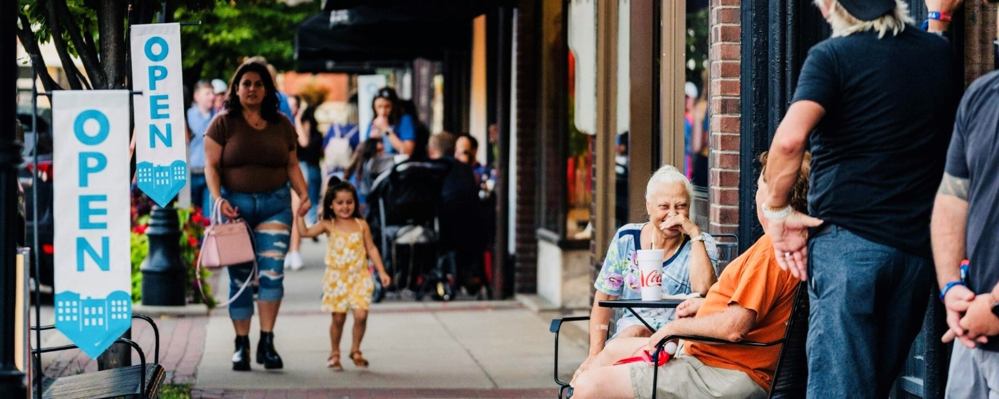 People walk, talk, and relax outside open businesses along a lively Main Street sidewalk in Bardstown, Kentucky.
