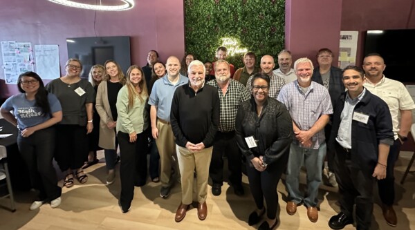 A large group of people poses for a photo in a room with pink walls