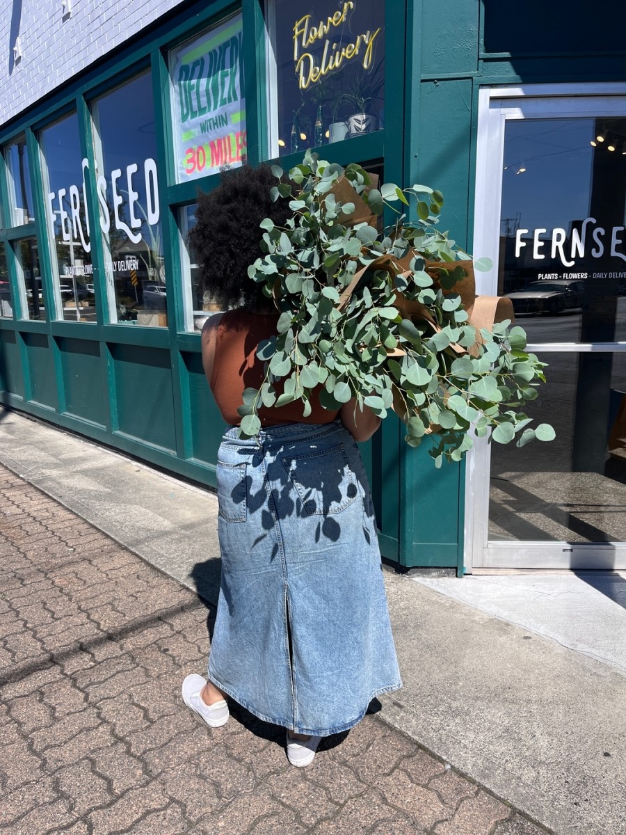 Woman holds large eucalyptus plant outside of shop windows