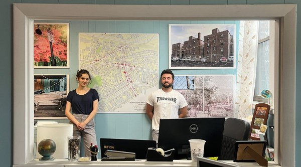 Two people standing in an office surrounded by pictures and maps depicting a downtown district