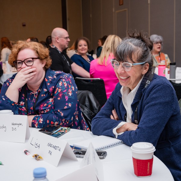 Two women sitting at a table laugh during a conference session