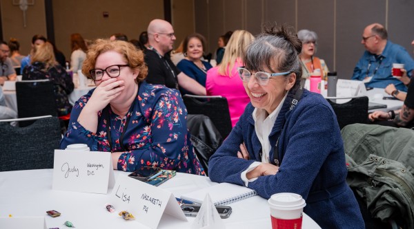Two women sitting at a table laugh during a conference session
