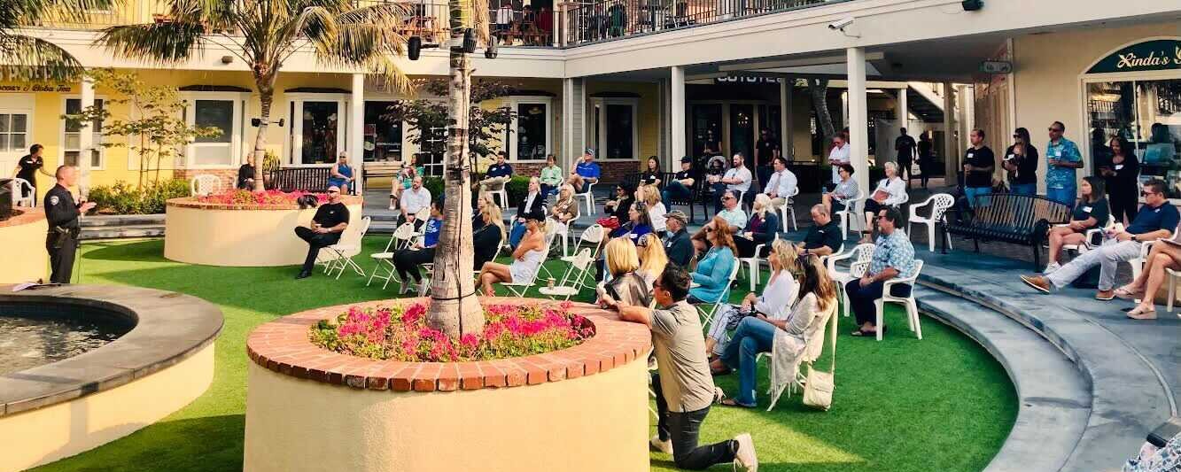 A large group of people seating on an outdoor grassy patio during a community meeting
