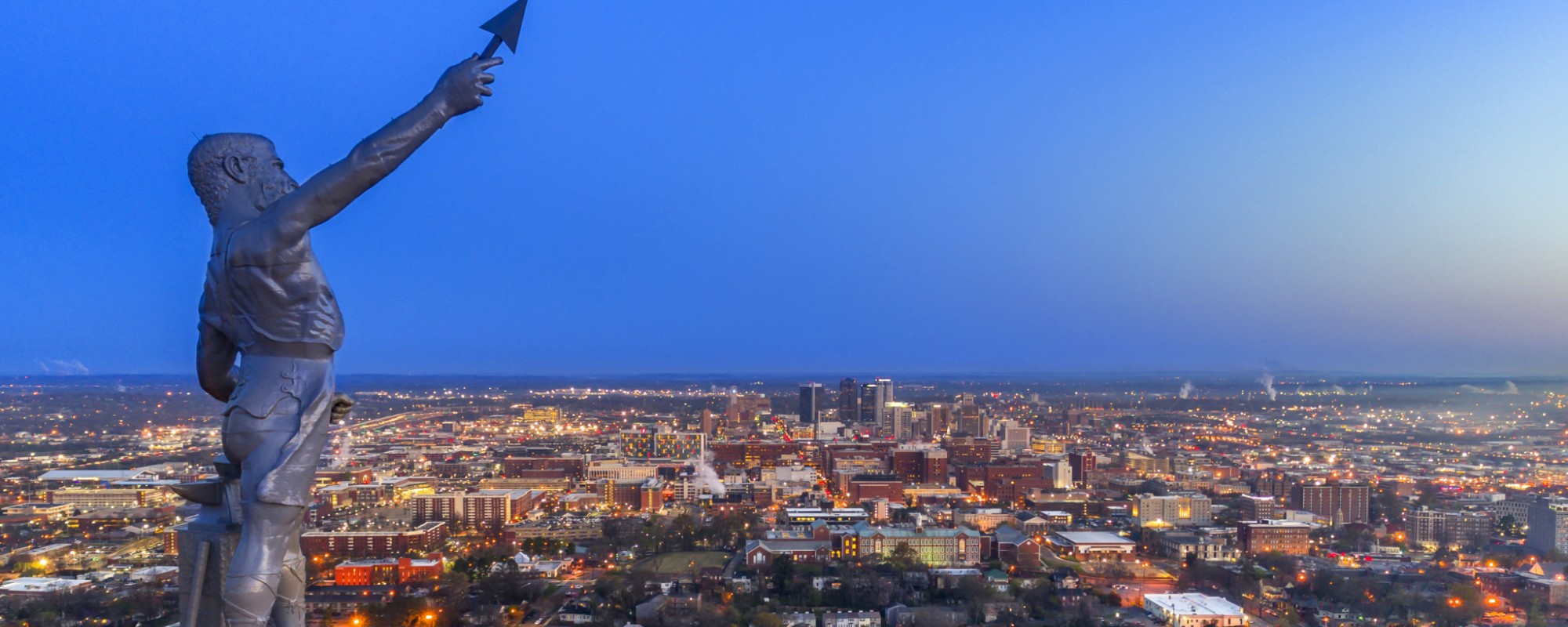 Vulcan Statue with illuminated city of Birmingham skyline in the background.