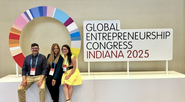 A man and two women pose in front of a sign with the logo for the 2025 global entrepreneurship congress.