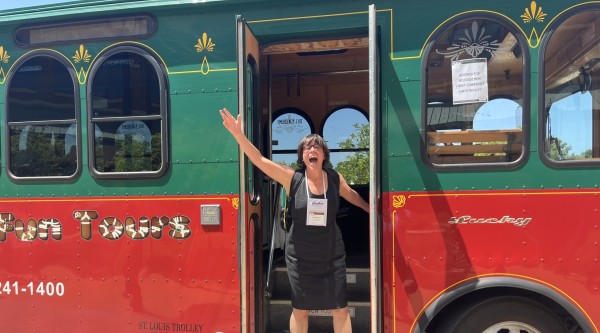 A woman stands in the door of a St Louis trolley and holds her hand up in the air