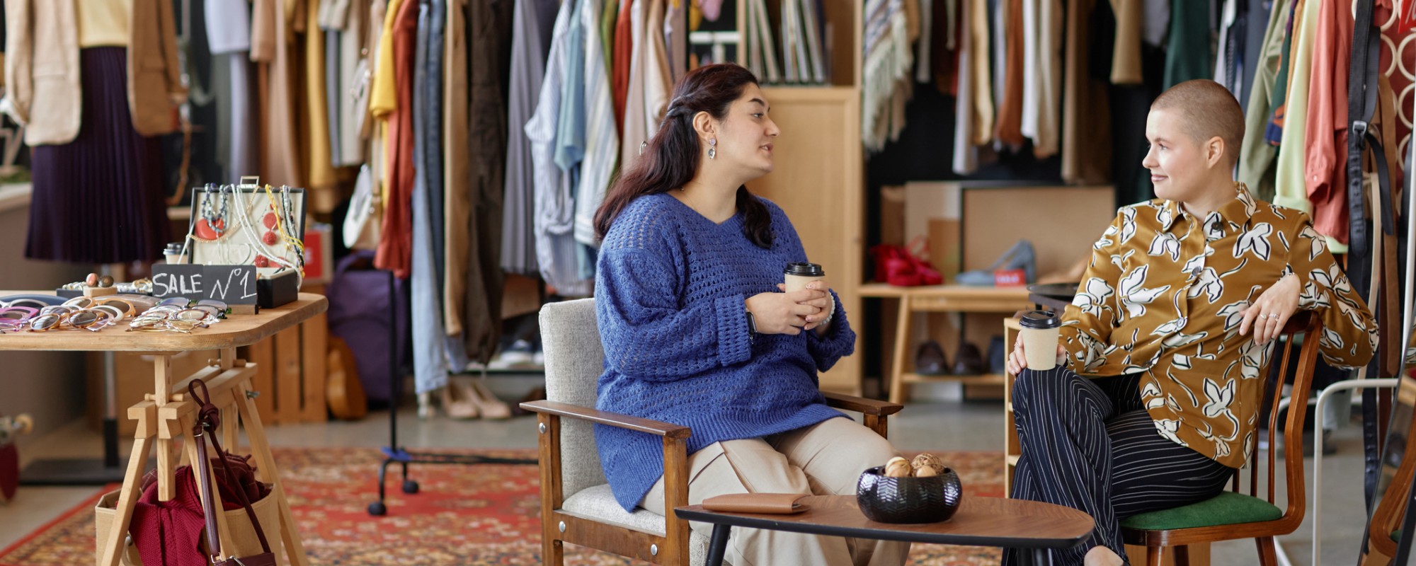 Two people sitting at a table drinking coffee inside a clothing store