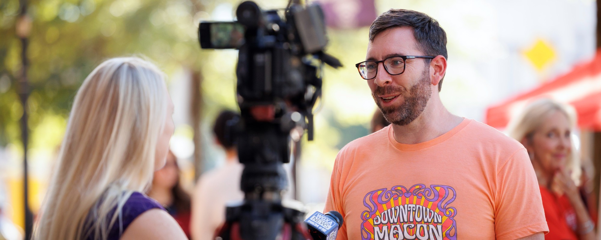 Man being interviewed by a reporter. News camera is in the foreground.