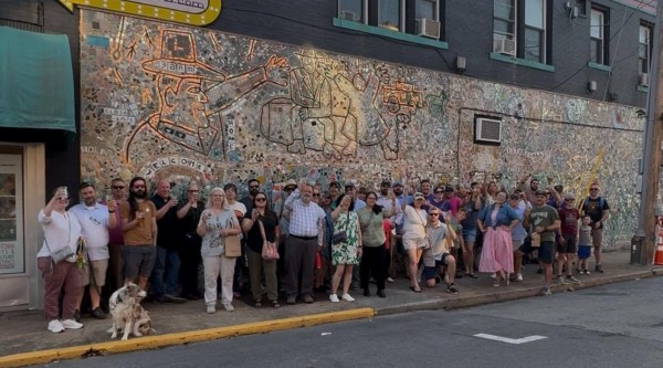 A large group of people pose in front of a mural