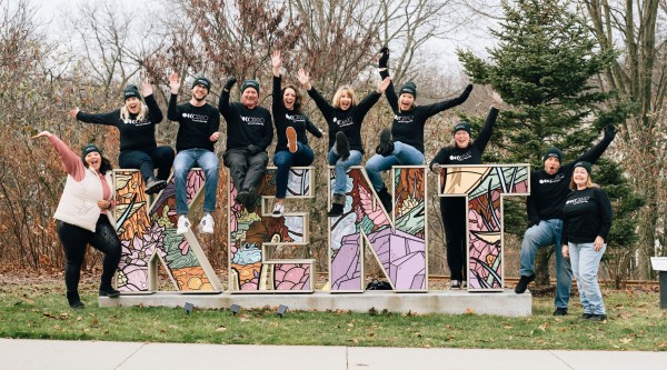 People striking celebratory poses while standing next to and sitting on top of artfully decorated letters spelling "KENT"