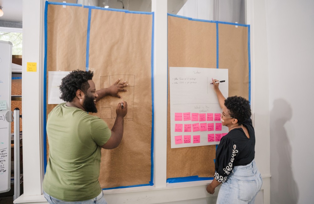 Two people smile at each other while writing on butcher paper taped to a window.