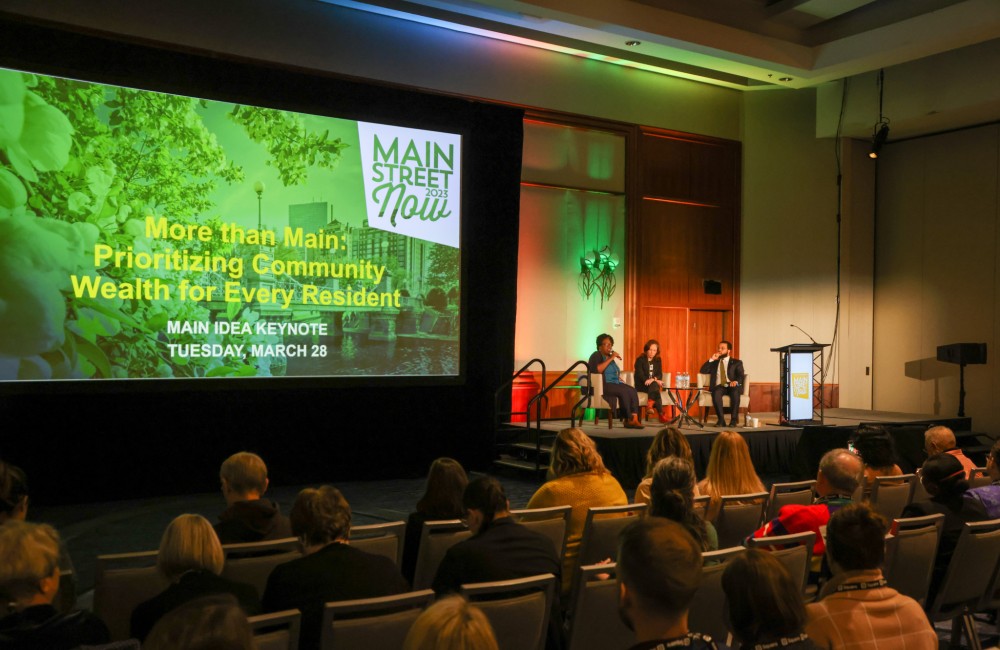 A panel of speakers present to a crowded room.