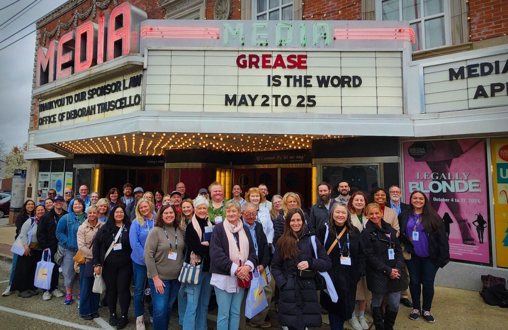 A large group of people pose for a photo in front of a historic theater marquee.