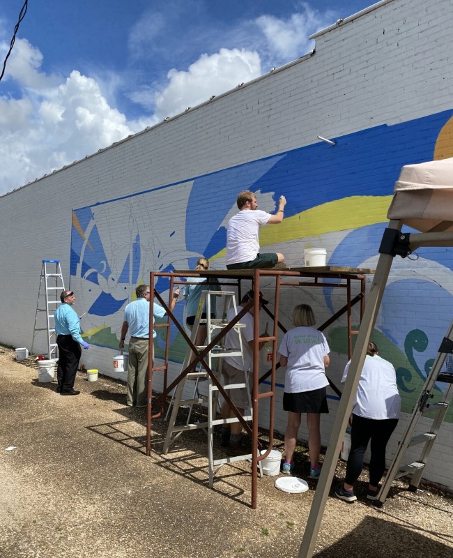 People painting a mural onto the exterior of a building.