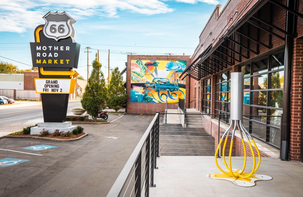 Entrance exterior of a food hall with a large yellow whisk sculpture and Route 66-inspired roadside sign.