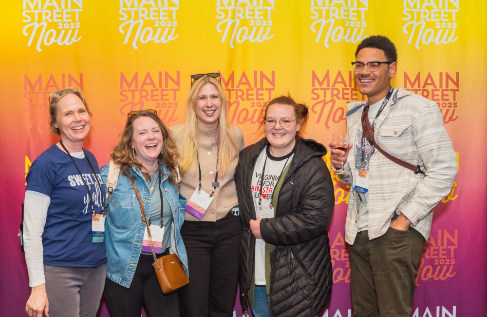 A small group of people smile while posing in front of a vibrant yellow, orange, and magenta step-and-repeat banner.