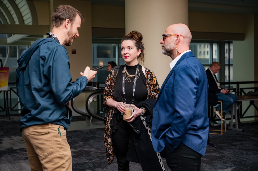 Three people chat while standing in a lobby.