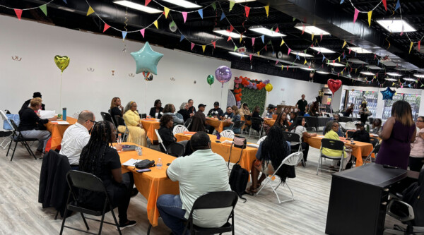 Tables of people at an event in a room decorated with pennants and balloons