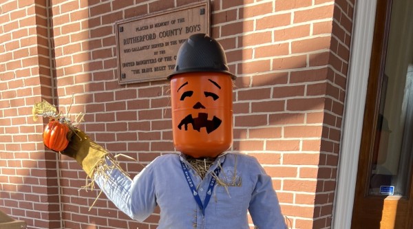A scarecrow in jeans and a blue shirt with a pumpkin head