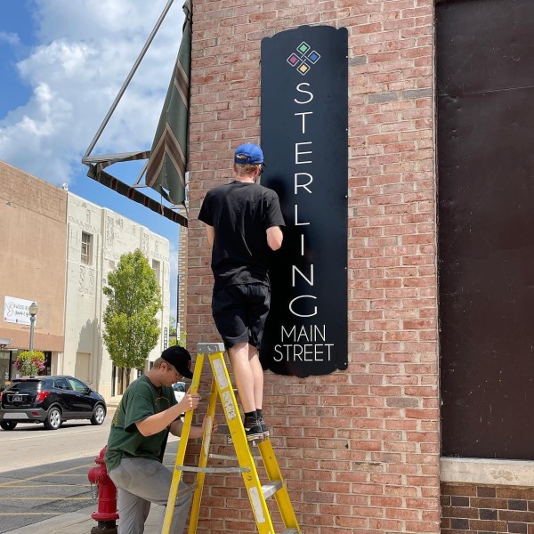 Installing a branded Main Street sign on a brick building in Sterling, Illinois