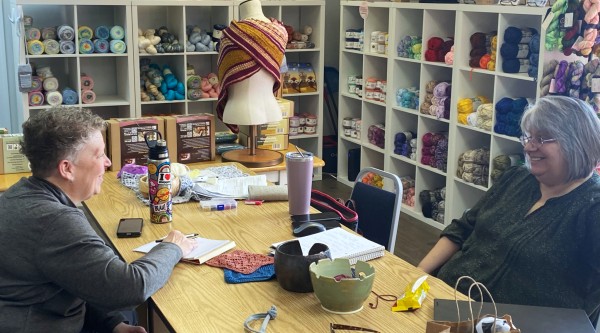 Two women sitting at a table in a colorful yarn shop