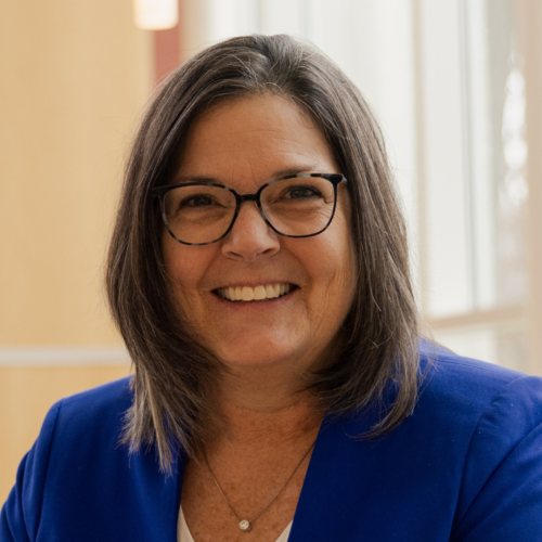 Woman with glasses wearing blue jacket smiles at camera