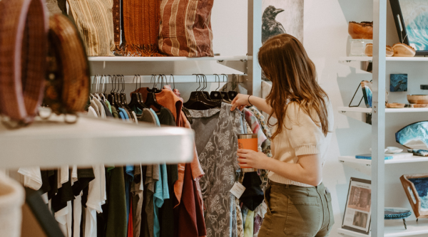Woman holding thermos looks at clothing in local shop.