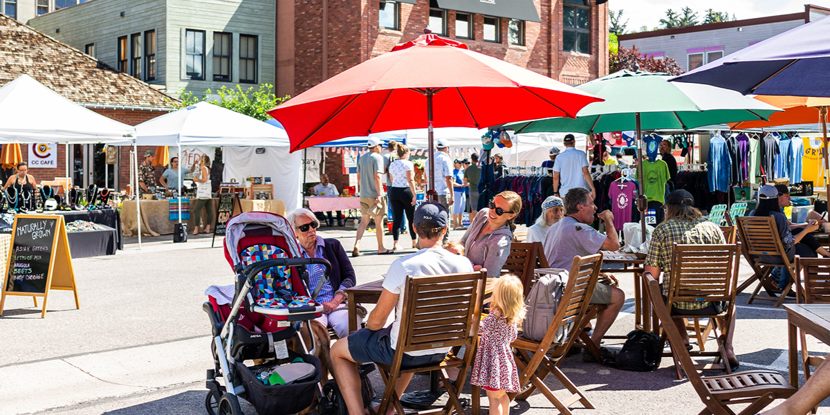 People sitting at tables and browsing stalls at an open streets event