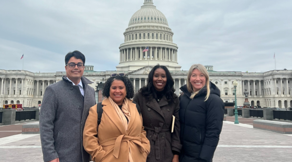 Four people posing for a photo in front of the Capitol building