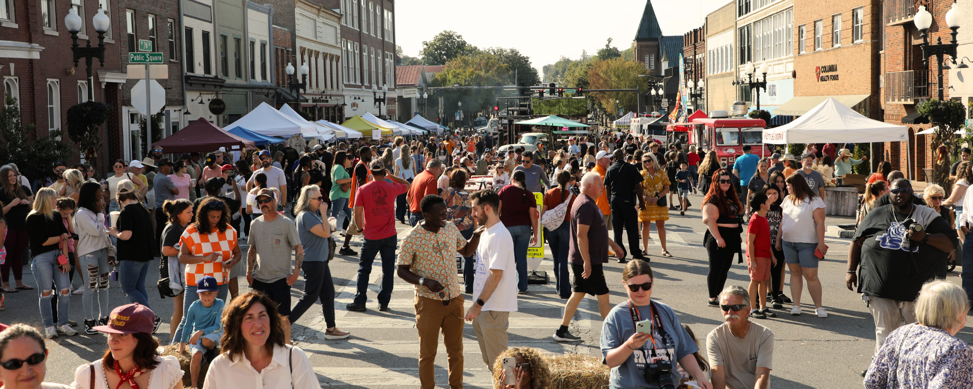 A large crowd of people at a downtown street fair on a sunny day