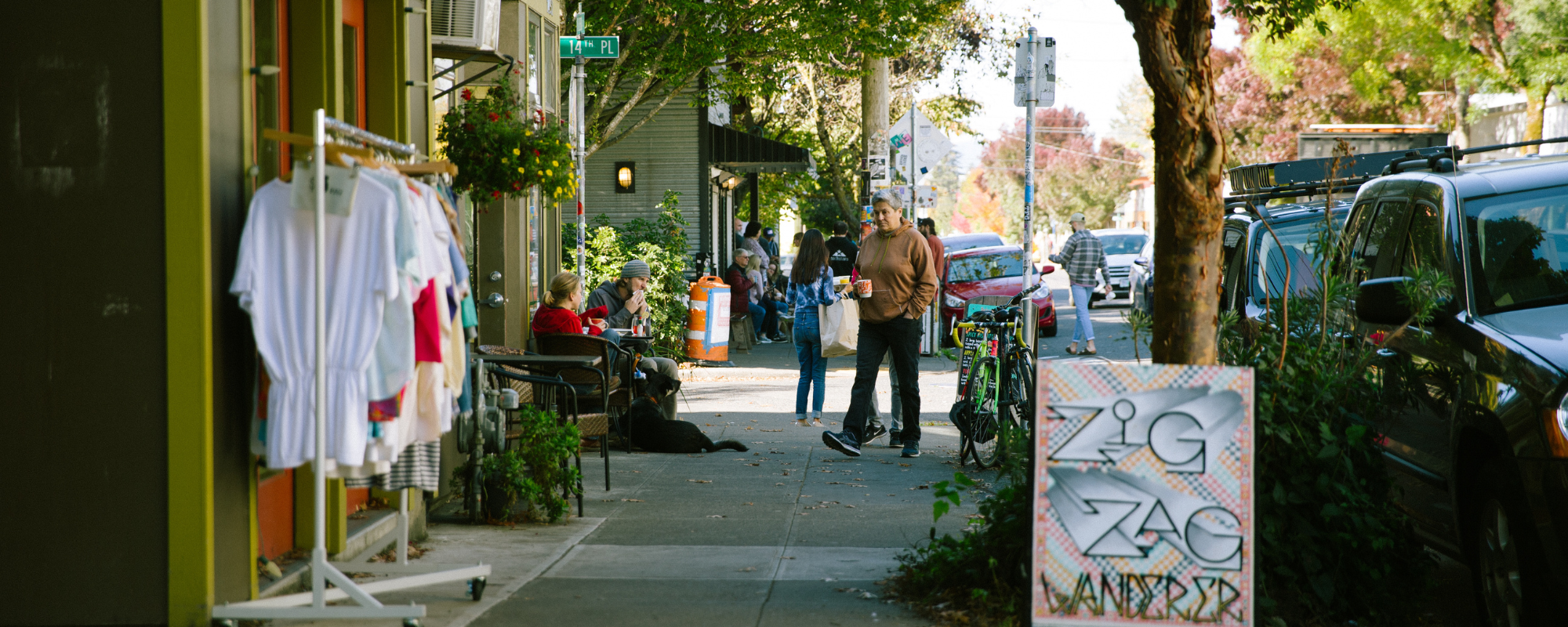 Sidewalk outside a small business with clothes for sale on a rack and a sandwich board advertising the business