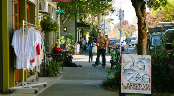 Sidewalk outside a small business with clothes for sale on a rack and a sandwich board advertising the business